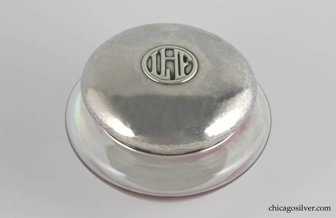 Kalo Jar for powder, two-piece, with glass bottom and separate sterling top.  Jar is hand-blown rainbow glass with flat bottom, flaring sides, cylindrical neck.  Tight-fitting silver lid is mushroom shaped, with some top centering an applied LHF mono inside a circle.  Bottom of the lid has applied wire around the rim.  Fairly heavy, and nice hammering.  Top:  4-3/8" W and 1-1/4" H.  Glass bottom:  5-1/4" W and 2-1/4" H.  Together:  5-1/4" W and 3-1/4" H.  Marked:  STERLING KALO
