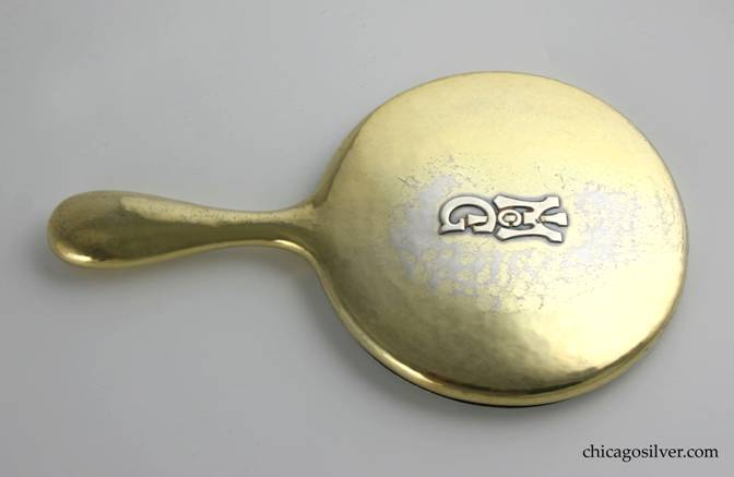 Kalo mirror, hand, with round silvered beveled-glass in round frame above bulbous handle with rounded end.  Covered with gold wash that is worn in places.  Applied McG mono on back.  Heavy and hammered.  9-3/8" L and 5-1/2" W and 5/8" D.  Marked:  STERLING KALO