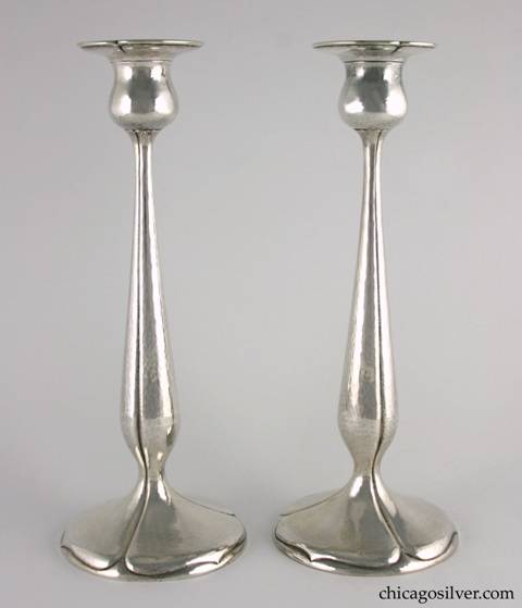 Kalo candlesticks, tall, pair (2), hammered surfaces with pedestal base, flat bottoms, and tulip form with fluted sides and spade shaped designs on base.  In green cloth KALO bags with yellow stitching.  12" H and 4-3/4" W across base and 2-7/8" W across top.  Marked:  Candlesticks:  STERLING / HAND WROUGHT / AT / THE KALO SHOP / S402.  Bags:  The Kalo Shop / Handwrought Silverware / Chicago
