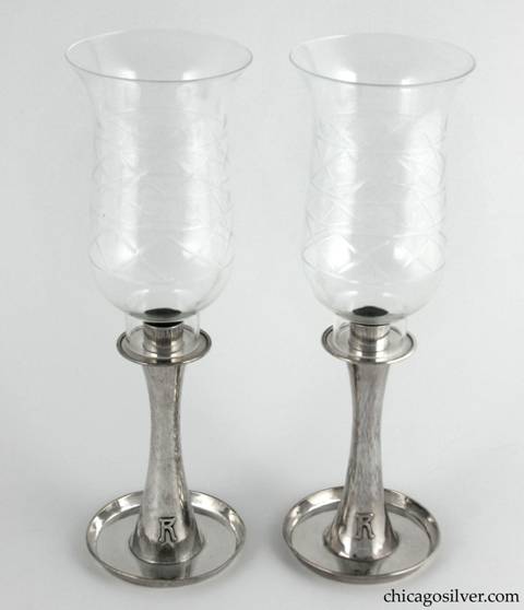 Kalo hurricane lamps, pair, composed of two candlestick bases plus two removable glass lamps.  The candlesticks have saucer-shaped bottoms with upturned rims, and taper up toward the middle then broaden out again at the top in a figure-8 shape.  The simple bobeche sits above a circular base for the glass lamps.  The tulip-shaped lamps are thin and delicate, and are covered with cut glass designs of two rows with and shapes alternating with lens-like dots.  Candlesticks have applied "R" monograms on outside of base.  Candlesticks:  3-3/4" W at bottom, 2" W at top and 6 H.  Lamps:  3-3/4" W and 6-1/2" H.  Together:  11-3/4" H.  Marked:  STERLING / HAND BEATEN / AT / KALO SHOPS / PARK RIDGE / ILLS. / 6197