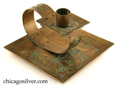 Carence Crafters candleholder, brass, composed of square tray with raised edges riveted to looping strap holding smaller square drip-tray and cylindrical riveted candle-holder.  Surfaces acid etched with floral design.