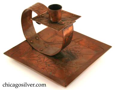Carence Crafters candleholder, copper, composed of square tray with raised riveted to looping strap holding smaller square drip-tray and cylindrical candle-holder.  Surfaces acid etched with floral design.