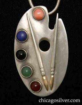 Laurence Foss pendant on chain, in the form of an artist palette, with notched side, five round bezel-set cabochon stones (carnelian, chrysoprase, onyx, lapis, and coral) representing paints, and two chased lifelike applied silver paintbrushes on either side of thumb hole with 14K gold brush tips.  Pin on back for use as brooch.  