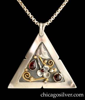 Laurence Foss pendant on chain, triangular, with fixed and chased bale at top.  Wide notched silver frame with corners that curve forward, around incised oxidized interior with gold beads and curving wires, and detailed applied silver leaf and blossom.  Bezel-set teardrop garnet on the left, round bezel-set garnet with notched frame on the right, and small round bezel-set garnet in the center of the blossom.  On box chain.  