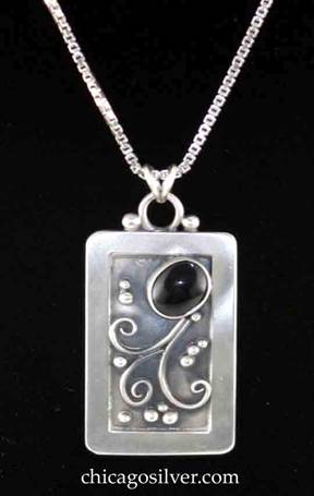 Laurence Foss pendant on chain, rectangular, with rounded corners and fixed round bale on top with small silver bead on each side.  Wide frame around incised oxidized interior with silver bead and curving wire ornament and dark black oval cabochon bezel-set stone at angle near top.  On Venetian box chain.  