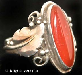 Laurence Foss ring, silver, with large slender oval vertical bezel-set cabochon carnelian stone in oxidized frame surrounded by an applied serrated leaf with a prominent central vein and beads and wirework decoration on each side.  A wire runs around the back of the ring connecting the bottoms of each leaf stem