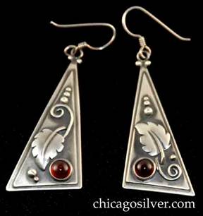 Laurence Foss earrings, pair (2), for pierced ears, with long wire hooks, slightly convex bodies in the form of long thin right-triangles with smaller triangle applied over slightly larger one.  Silver bead and curving wirework ornament on oxidized background and applied leaf with strong central spine and spiraling stem.  Deep red cabochon bezel-set garnet stone at one corner.