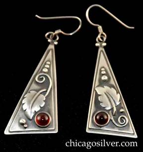 Laurence Foss earrings, pair (2), for pierced ears, with long wire hooks, slightly convex bodies in the form of long thin right-triangles with smaller triangle applied over slightly larger one.  Silver bead and curving wirework ornament on oxidized background and applied leaf with strong central spine and spiraling stem.  Deep red cabochon bezel-set garnet stone at one corner.