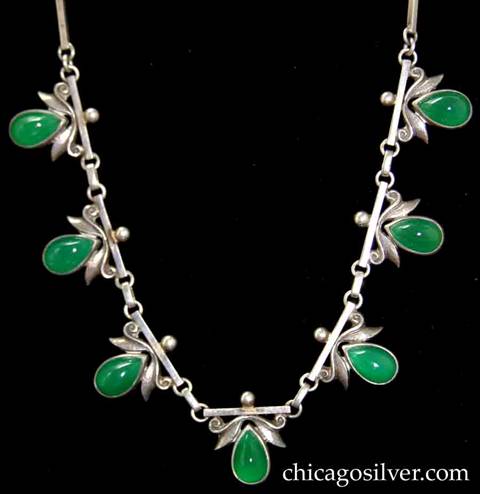 Laurence Foss necklace composed of ten bar links and seven links with teardrop-shaped green bezel-set cabochon stones below scrolling ornament with stylized leaves, and small bead at very top.   Links with stones and intermediate links are bar-shaped and joined to each other with small round silver loops.  