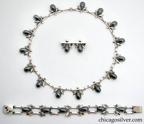 Laurence Foss set consisting of necklace, link bracelet, and pin, all with bezel-set teardrop cabochon hematite stones each with a stylized silver leaf and scroll at the point of the teardrop.  Leaf details above the stones are hand-worked.  All pieces are heavy.  This piece was made while Foss was working at Georg Jensen.
