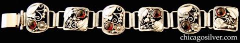 Laurence Foss bracelet, large, with garnets.  Three square open links alternating with three oval-sided ones, each slightly convex and with a large round bezel-set deep red cabochon garnet in one corner.  Surrounding the stones are stylized blossoms, leaves, beads, and open wirework scrolls.  While all Foss bracelets are handsome, this one is especially lovely, and is very much like the work of Oakes.  