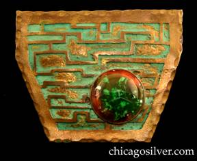 Frost Workshop brooch, brass, shield-shaped with six straight sides, with a wide top and narrow bottom, gilded hammered edge, and a gold maze of narrow lines against a blue-green verdigris background with applied splotches of gilding, and a large round bezel-set red and green glass cabochon stone in the lower right-hand corner.