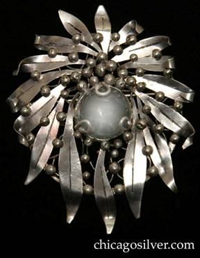 Mary Gage pin, round, composed of a wreath of long, thin outward-pointing chased leaves on a circular frame strengthened with irregular wirework beneath centering a large clear bezel-set rock crystal stone surrounded by several dozen silver beads atop and between the leaves