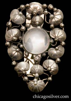 Mary Gage dress clip, tapered shield-shaped form centering a round bezel-set clear rock crystal stone surrounded by small chased lily pads, vines, and applied silver beads