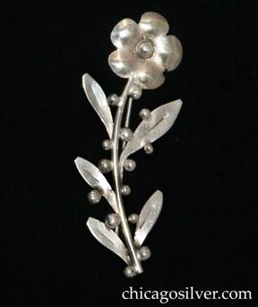 Mary Gage brooch / pin, flower form, composed of a five-petal blossom with central bead atop curving stem with five leaves and numerous applied silver beads.
