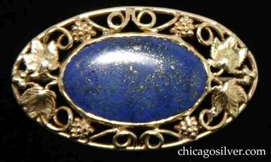 Frank Gardner Hale brooch, gold, with lapis.  Oval form with a ring of applied grape leaves, bunches of grapes, and curling wire decorations centering a large flat oval lapis stone with silver inclusions.