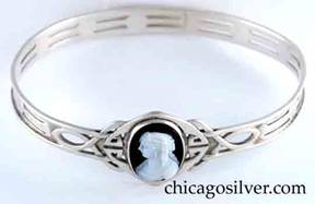 Kalo bracelet, bangle, with oval white cameo of woman facing left on a black background, on an elaborate wirework Celtic knot with small internal cutouts, with two repeated pairs of trapezoidal cutouts encircling the band, and applied wire to the top and bottom of the band.