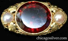 Brooch, by Edward Oakes, handwrought 14K gold, oval 14K gold frame with large, faceted orange-red hessonite garnet, flanked by two pearls set among delicate hand made leaves, tendrils and beads.  Raised gallery.  Beautifully crafted with great detail.
