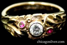 Ring, by Gilbert Oakes, hand wrought in 14K gold with central faceted diamond, flanked by two small rubies and two simple applied leaves with bead work.  Textured background.