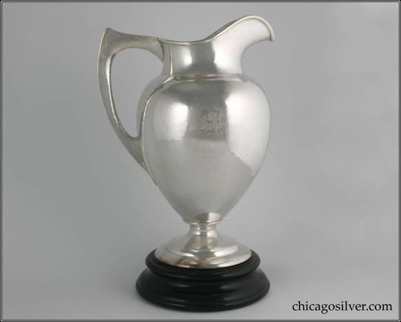Kalo pitcher, water, large on turned black wood plinth.  Tall, hammered vase form on high circular foot.  Rounded shoulder with tapered neck and high spout.  Flat edge hollow handle.  Double engraved monograms "EJV" and "BMM" (The EJV is for Evelyn Vernon Johnson of Princeton, NY -- family of the Johnson & Johnson Pharmaceutical Co.) Black wood plinth onto which the pitcher securely attached via 1/4 turn.  11" H and 8-1/4" W
12-3/4" H and 8-1/4" on plinth.  STERLING / HAND WROUGHT / AT / THE KALO SHOP / E609 / 5 PINTS
