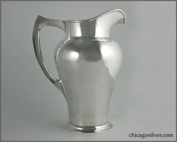 Kalo pitcher, tall, on spreading foot, with narrow bottom flaring to bulbous shoulder, tall cylindrical neck with high arching spout, flat angular hollow harp-shaped handle that comes to a point in the corner.  Applied wire to rim and nicely hammered surfaces.  10" H and 7-7/8" W.  STERLING / HAND WROUGHT / AT / THE KALO SHOP / E508 / 5 PINTS