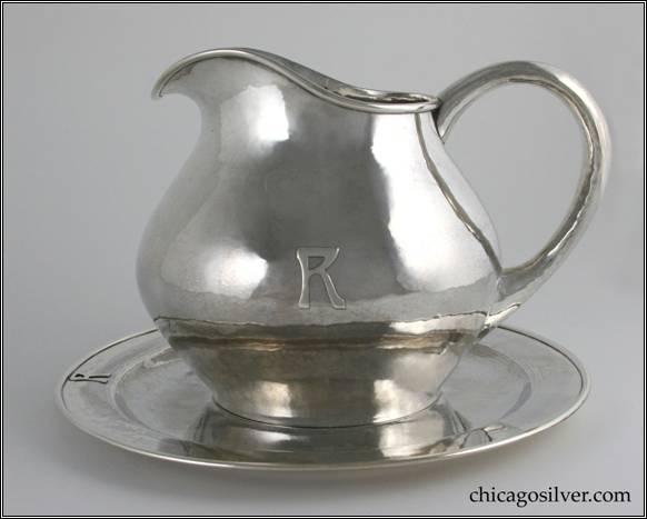 Kalo pitcher, water, and matching undertray.  Pitcher, low, squat form with central bulge, body tapers at rim with a gracefully formed spout.  Looping hollow handle.  Round undertray with slightly raised border and heavy, applied wire on rim.  Both pieces have applied letter R monogram.  Opposite monograms on both pieces is an engraved family crest of an arm, from the shoulder down in armor with a dagger in the closed hand.  Quite heavy.  Pitcher:  6-1/2" H and 8-1/2" W.  Undertray:  10" in diameter.  STERLING / HAND BEATEN / AT / THE KALO SHOPS / PARK RIDGE / ILLS.