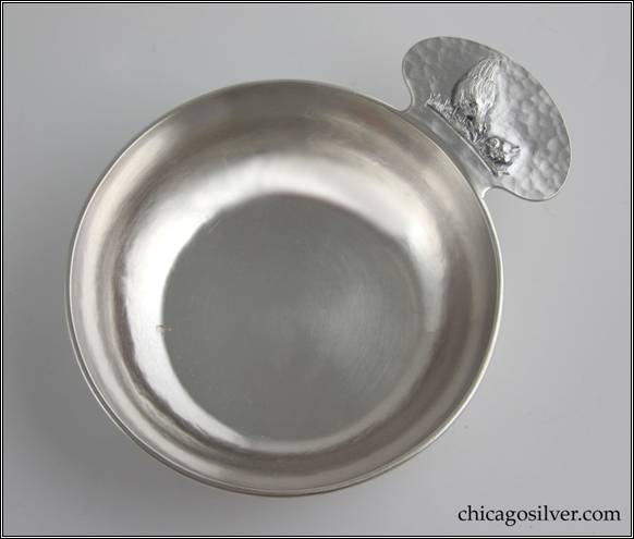 Kalo porringer, round, flat bottom form with rounded tab handle and applied wire rim.  Handle has chased and repoussé decoration of hen standing on grass beside small chick.  