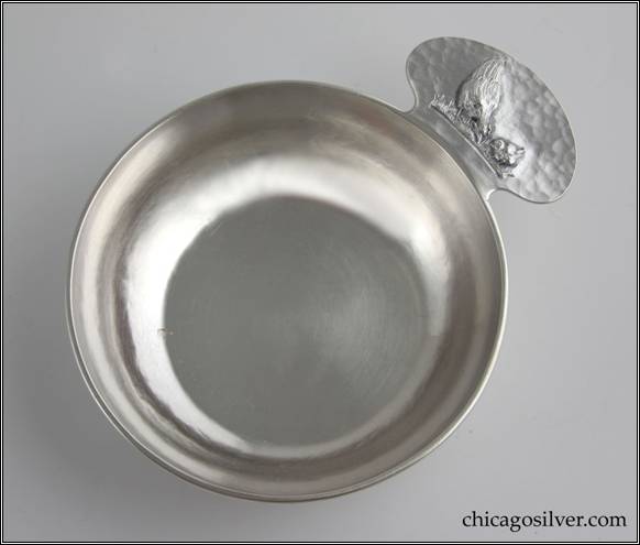 Kalo porringer, round, flat bottom form with rounded tab handle and applied wire rim.  Handle has chased and repouss decoration of hen standing on grass beside small chick.  