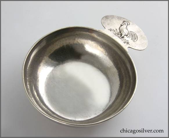Kalo porringer, round, flat bottom form with tab handle and applied wire rim.  Handle has chased and repoussé decoration of rooster standing on grass.  