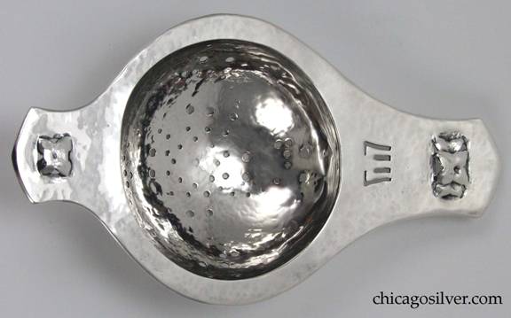 Rokesley tea strainer with short slightly pointed tab handle at one end, and longer one at the other.  Round bowl with spiral pierced design of large and small holes.  Pierced and repouss floral designs at each end, and small pierced geometric fork-like design at on the larger tab handle.  Heavily hammered surfaces.