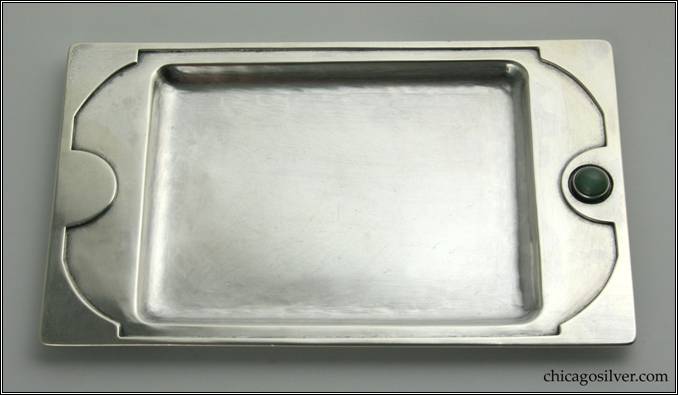 Kalo tray with stone, early.   Rectangular form with recessed rectangular center and raised edge that is wide at the ends.  Edge has applied border with curving cutout design and a central semi-circular lobe at each end, one of which centers a round bezel-set dark green cabochon stone.  Rounded corners on edges and recessed center portion.  6-3/4" L and 4-1/8" W.  Marked:  STERLING / HAND BEATEN / AT / KALO SHOPS / PARK RIDGE / ILLS.
