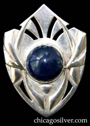 Art Silver Shop brooch / pin, shield-shaped, with sides that curve down gently to a point on the bottom, and upward with a slightly concave curve to a point at the top.  Applied tusk-shaped forms over curving saw-pierced details, centering an oval bezel-set blue cabochon lapis or sodalite stone.