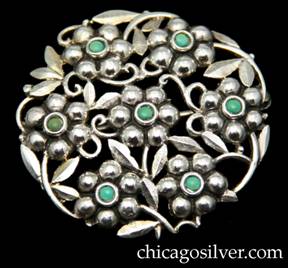 Brooch / pin, silver, with turquoise stones, European 935 silver.  Round frame with six repouss blossoms arranged in a circle with a seventh one at center, each blossom centering a small round bezel-set cabochon turquoise stone.  Blossoms are connected by silver leaves and curving stems.