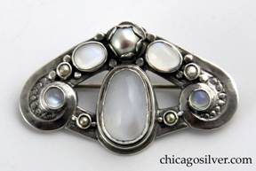 Unsigned brooch / pin, silver, with moonstones and pearls.  Roughly triangular in shape, with the top two sides curving down and ending in small spirals centering round moonstones, connected to a large central oval bezel-set moonstone with angled supports.  Two other oval moonstones flank a large pearl at the top set in a scalloped bezel, and have two smaller pearls below them.  Piece is decorated with rows of silver beads that have had the tops flattened.  