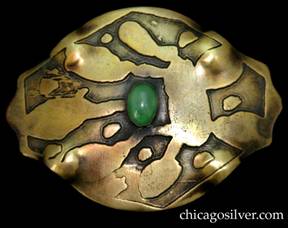 Pin, brass, large, freeform oval shaped, with acid-etched geometric design and oxidized background centering bezel-set green oval stone.  Four repousse bulges at the corners.